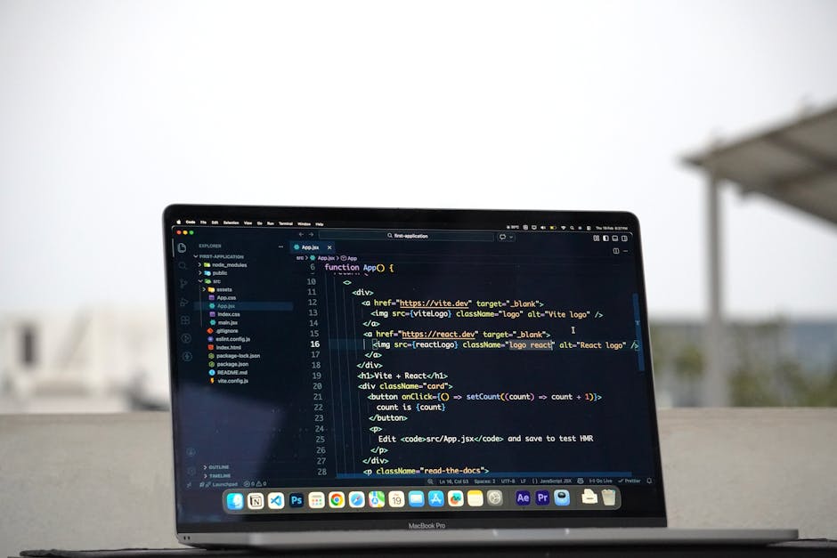 The image shows a MacBook Pro laptop placed outdoors on a flat surface, displaying a dark-themed coding interface with visible lines of HTML and JavaScript code related to a web application. In the ba